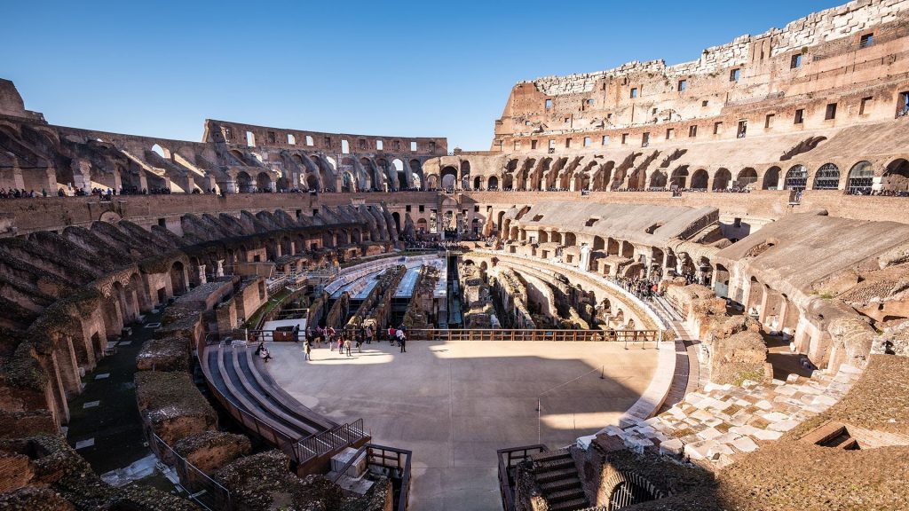 Interior view of the Colosseum in Rome, showing ancient stone arches, tiered seating, and the arena floor
